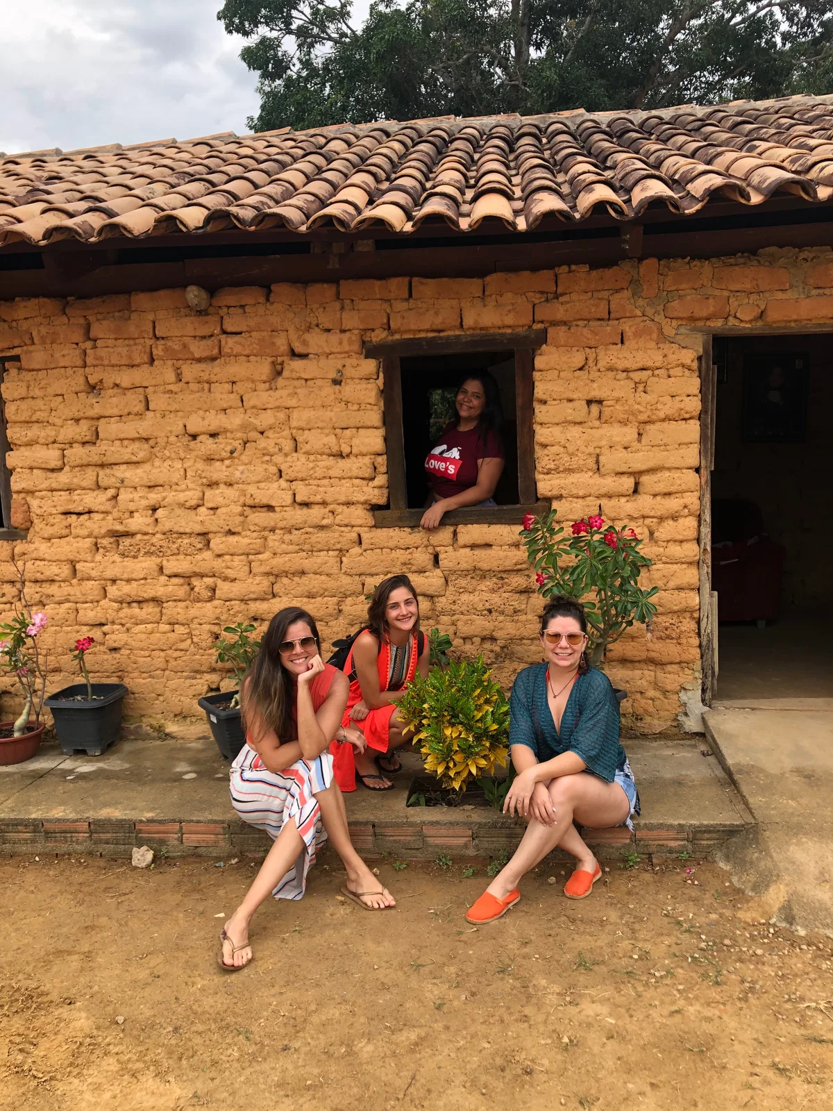 Dona Minervina en la ventana de su casa de adobe, con viajeras sentadas en el porche